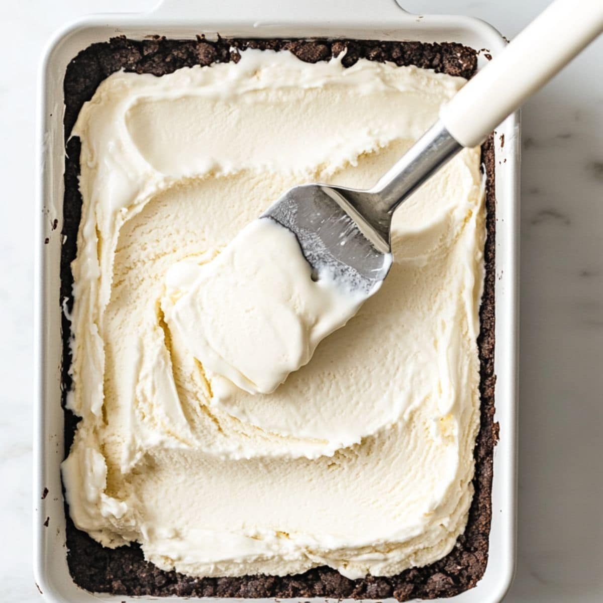 Cookie crust and vanilla layer being built, top-down with spatula
