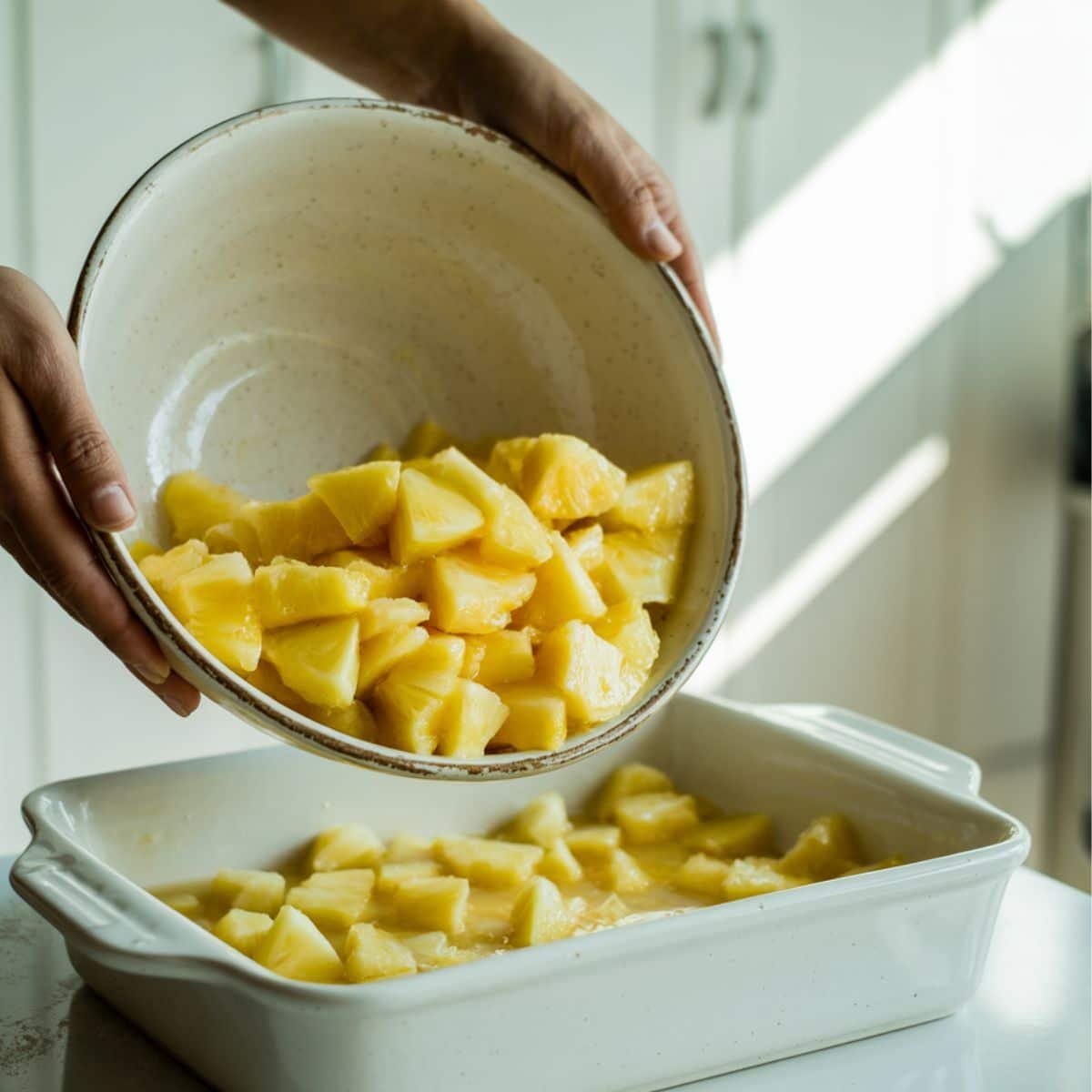 Crushed pineapple being added into a baking dish on a white counter