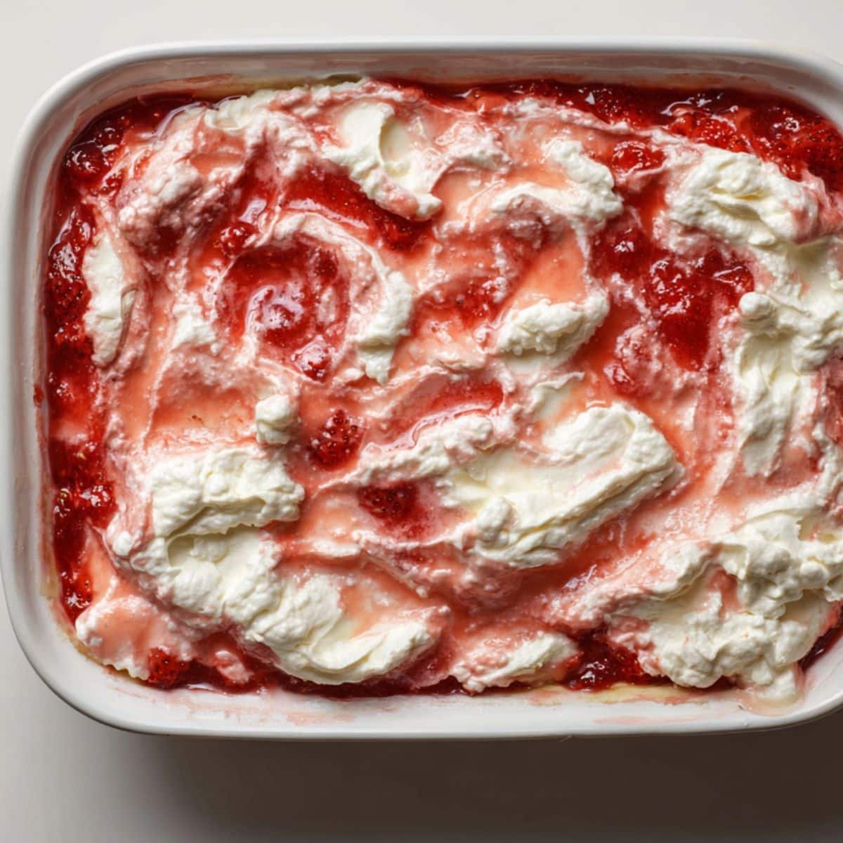 Spoon dollops of cream-cheese mixture swirled into strawberry base in the baking dish.	