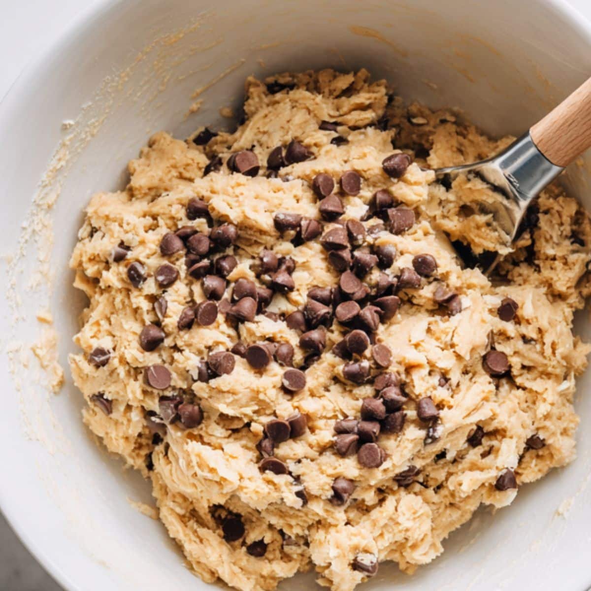 Stirring oats and chocolate chips into cookie dough on white countertop	