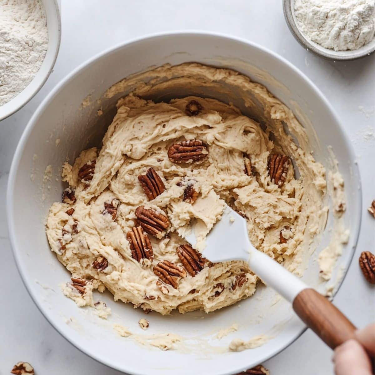 Cookie dough being mixed with toasted pecans in white bowl	