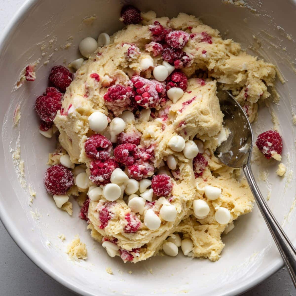 Cookie dough with raspberries and white chocolate chips being folded in	