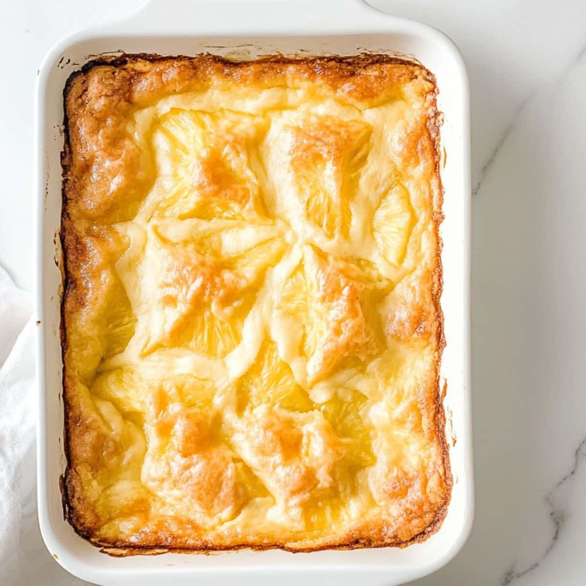 Golden baked pineapple dump cake resting in white dish on kitchen counter