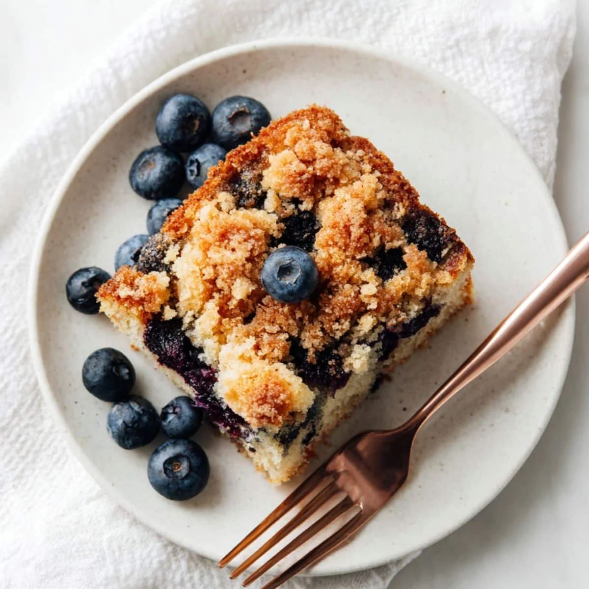 A slice of homemade blueberry sour cream coffee cake on a white plate	