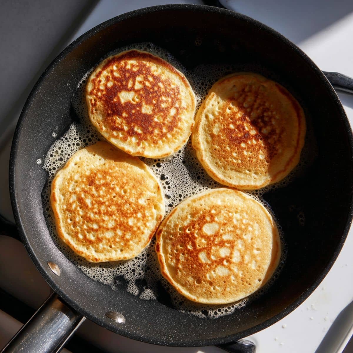 Oat flour pancakes cooking on a non-stick pan with bubbles on top	