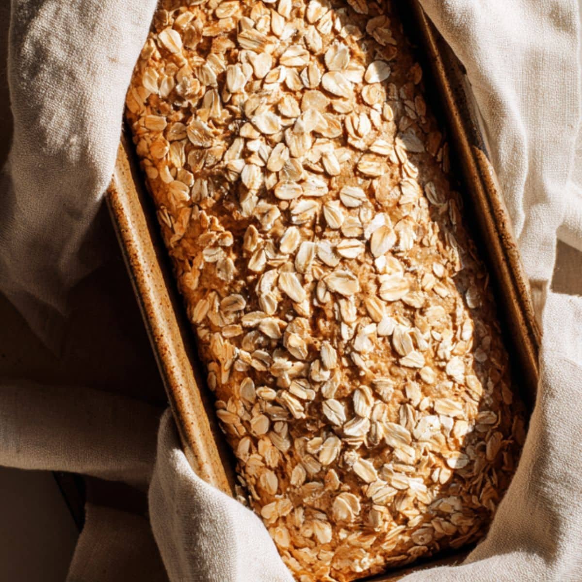 Oatmeal flour bread rising in a pan with oats sprinkled on top	