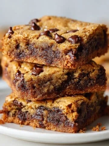 Stack of gooey chocolate chip cookie bars on white plate