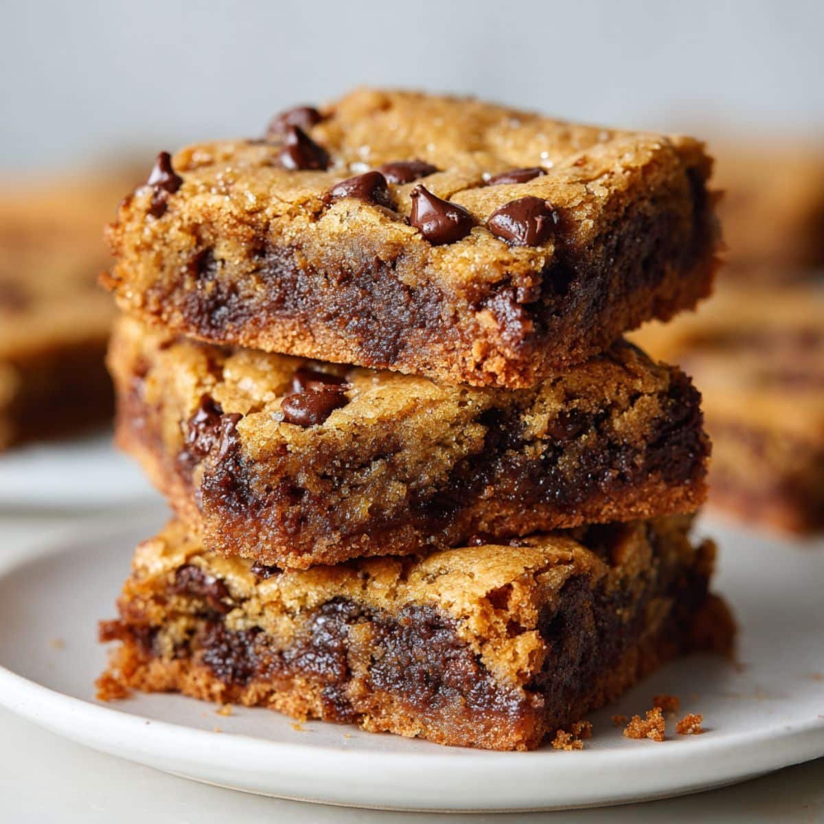 Stack of gooey chocolate chip cookie bars on white plate	