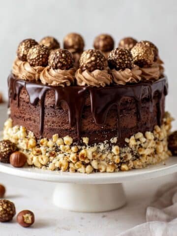 Homemade Ferrero Rocher cake with chopped hazelnuts and chocolate frosting on white cake stand