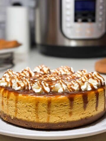 Homemade Instant Pot pumpkin cheesecake topped with caramel and chocolate drizzle on a white counter