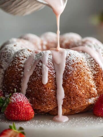Strawberry pound cake on a white plate, drizzled with pink glaze, styled casually with fresh berries
