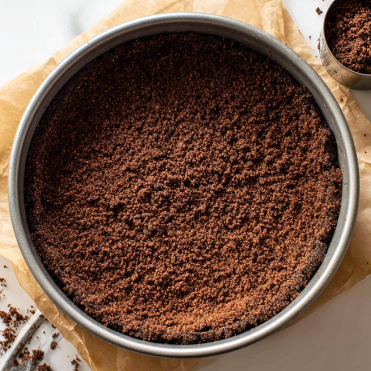 Pressing chocolate graham cracker crust into a springform pan.	