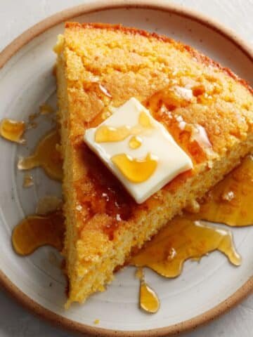 A warm slice of gluten-free cornbread topped with melting butter and drizzled honey