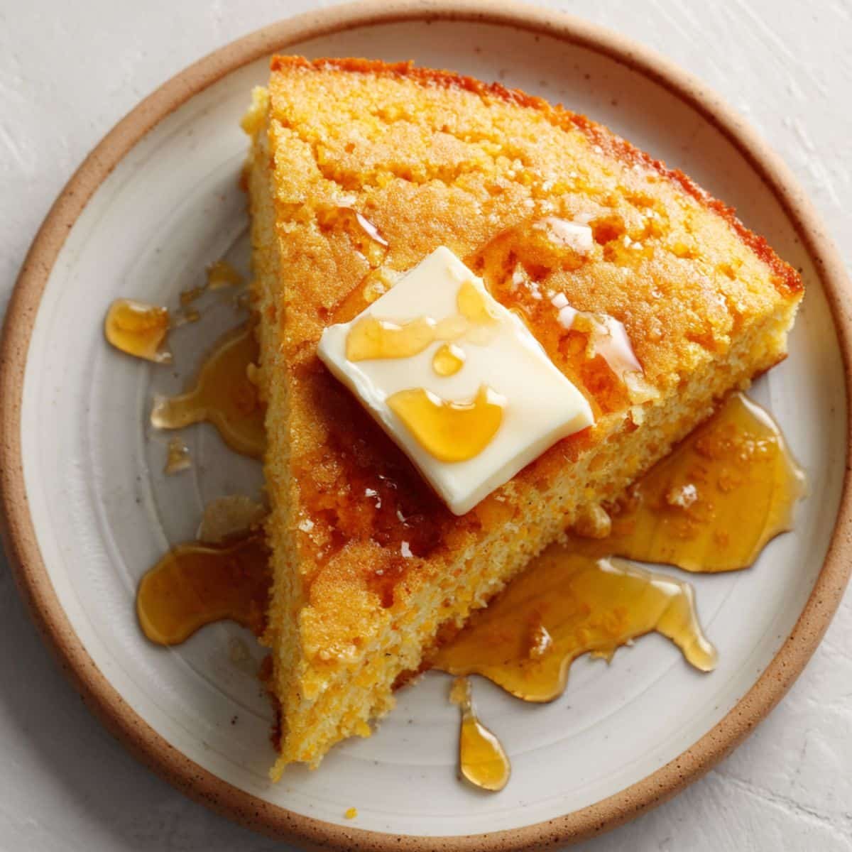 A warm slice of gluten-free cornbread topped with melting butter and drizzled honey