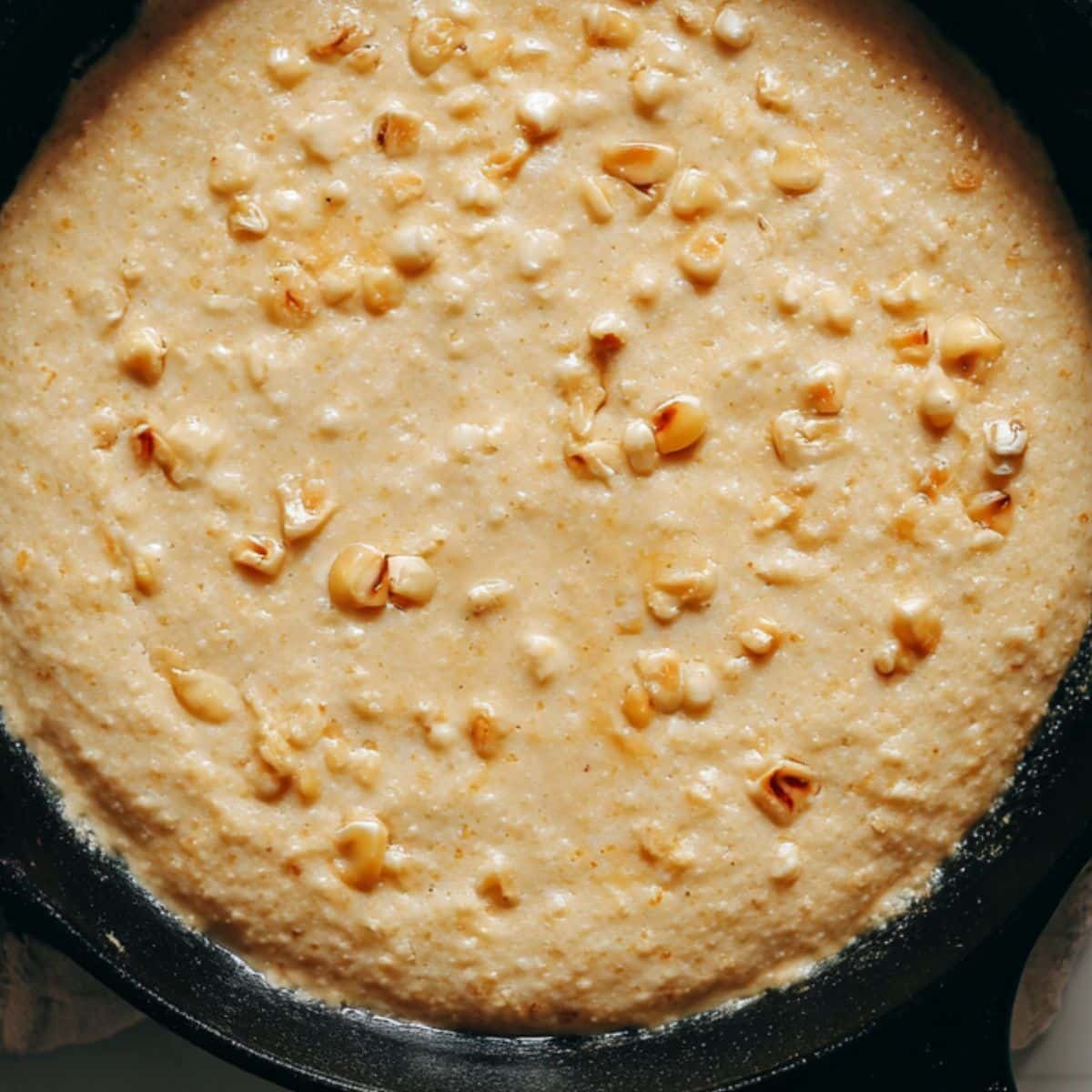 Pouring cornbread batter into a greased cast iron skillet with corn and cheese