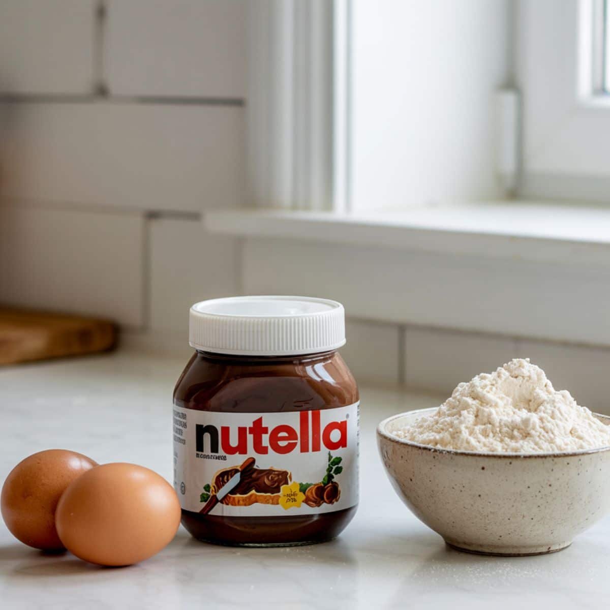 Nutella, eggs, and flour arranged on a white kitchen counter	
