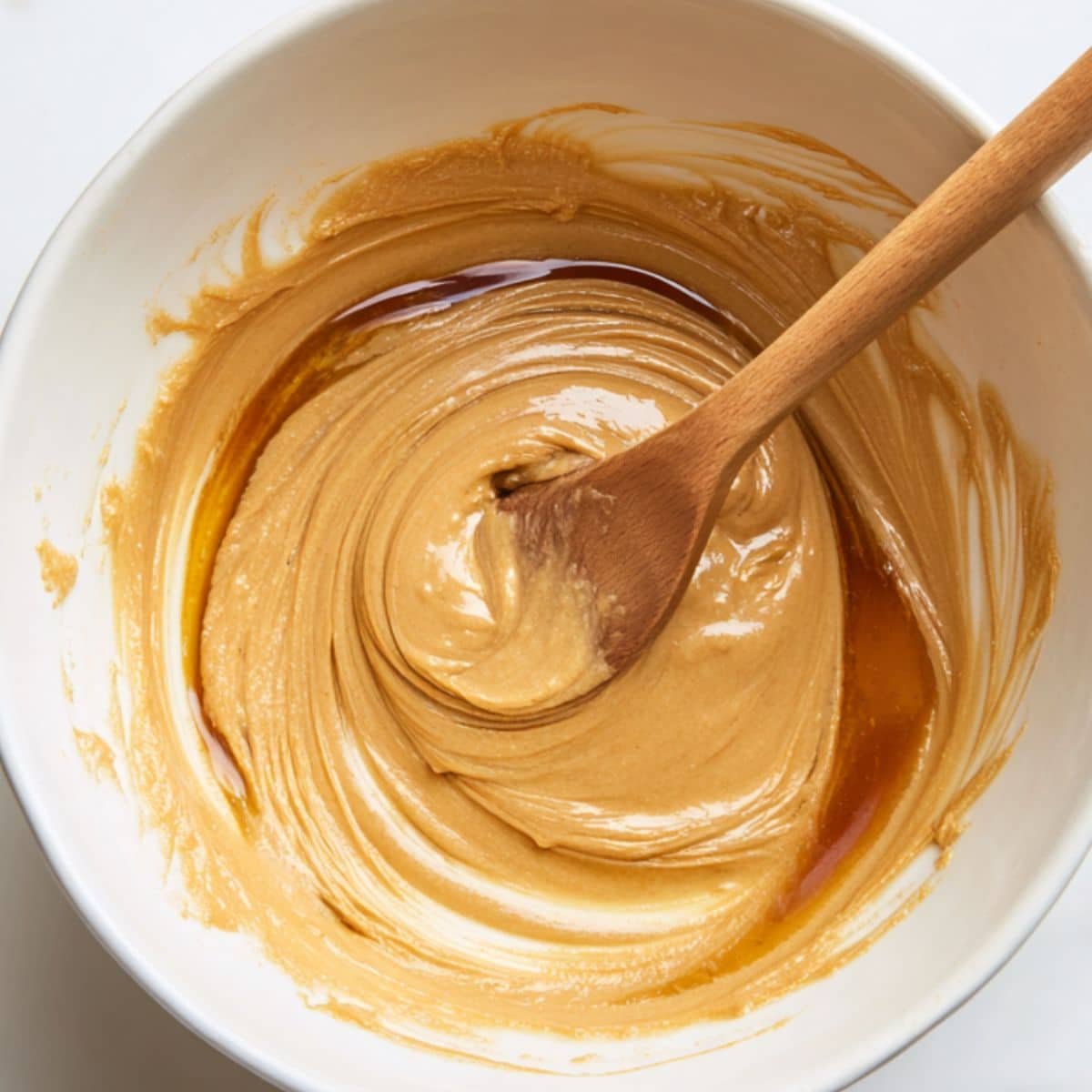 Mixing peanut butter and maple syrup in a white bowl for no bake oatmeal cookies	