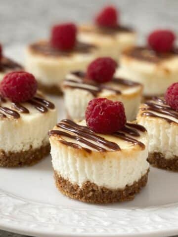 Plate of no bake cheesecake bites topped with fresh raspberries on a white kitchen counter