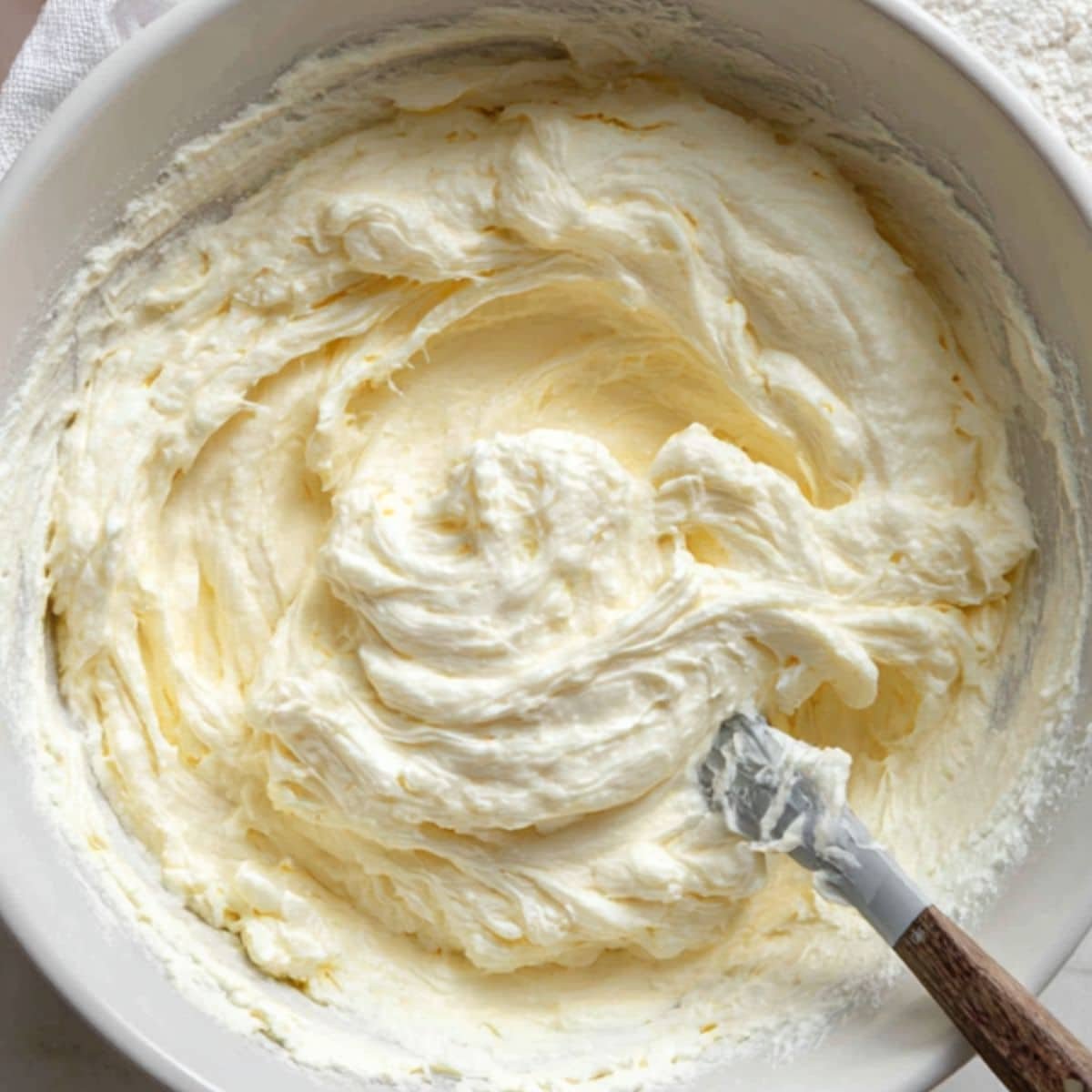 Whipped cream folded into cream cheese mixture in a mixing bowl on white counter	
