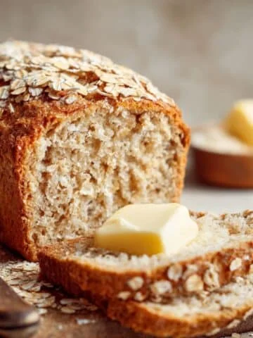 Slice of homemade oatmeal flour bread with butter on a wooden board