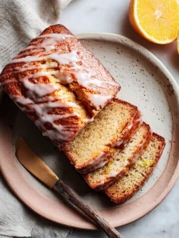 Homemade orange bread with glaze cooling on white counter
