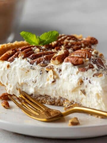 A generous slice of pecan cream pie on a plate with creamy filling and crunchy pecans on top