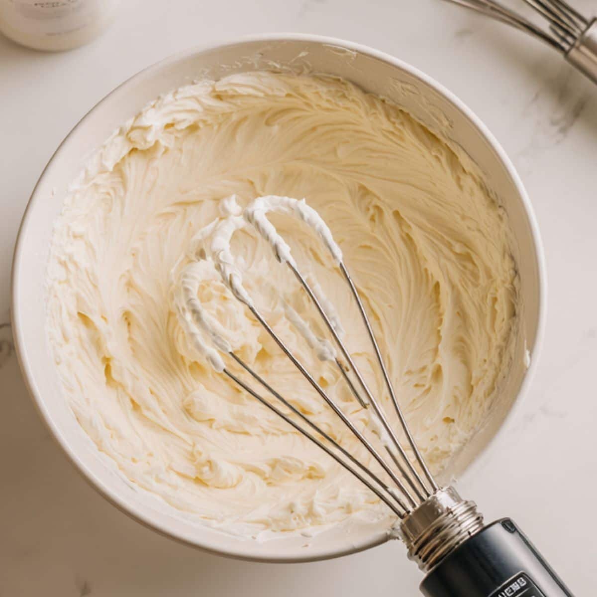 Cream cheese mixture being whipped with mixer in a large mixing bowl	