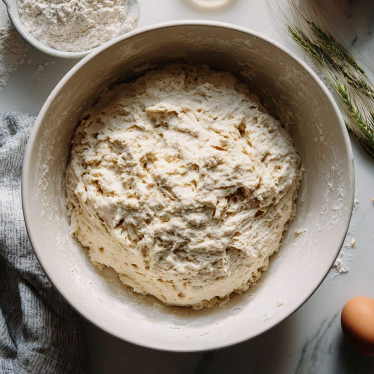 Hand mixing sourdough dough in a white bowl on a kitchen counter