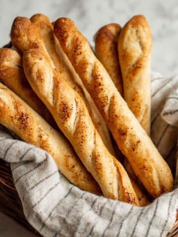 Golden homemade sourdough breadsticks in a basket on a kitchen towel