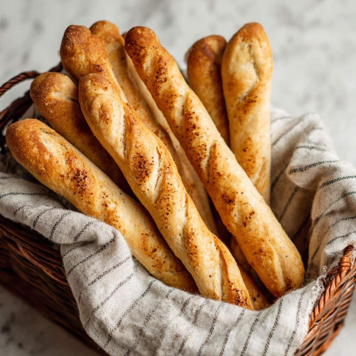 Golden homemade sourdough breadsticks in a basket on a kitchen towel	