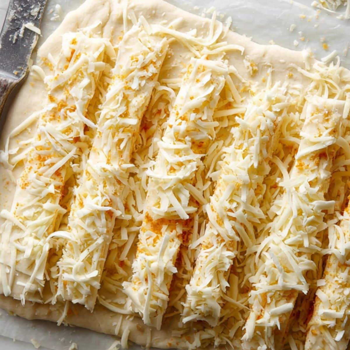 Sprinkling cheese and cutting dough into strips	