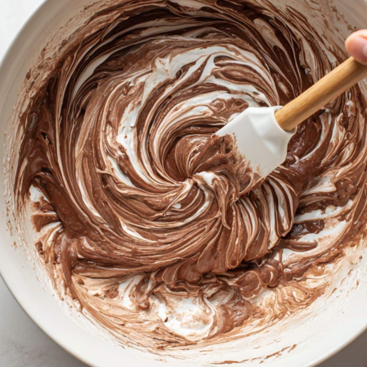 White spatula folding whipped egg whites into mocha batter in white bowl	