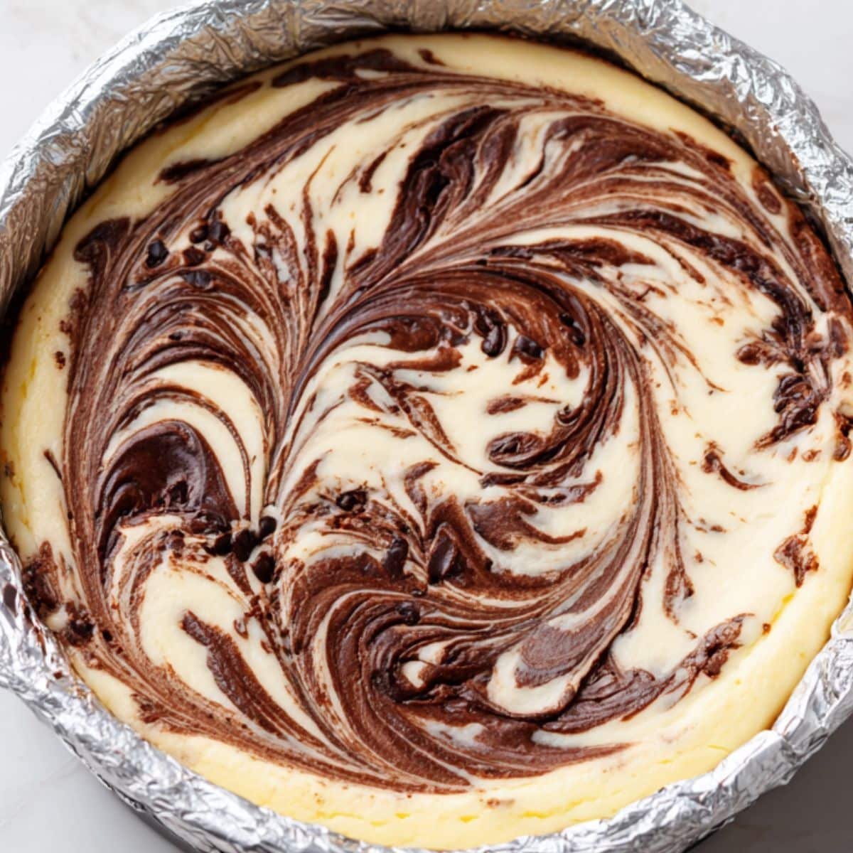 Cheesecake filling being swirled with chocolate using a knife inside the springform pan	