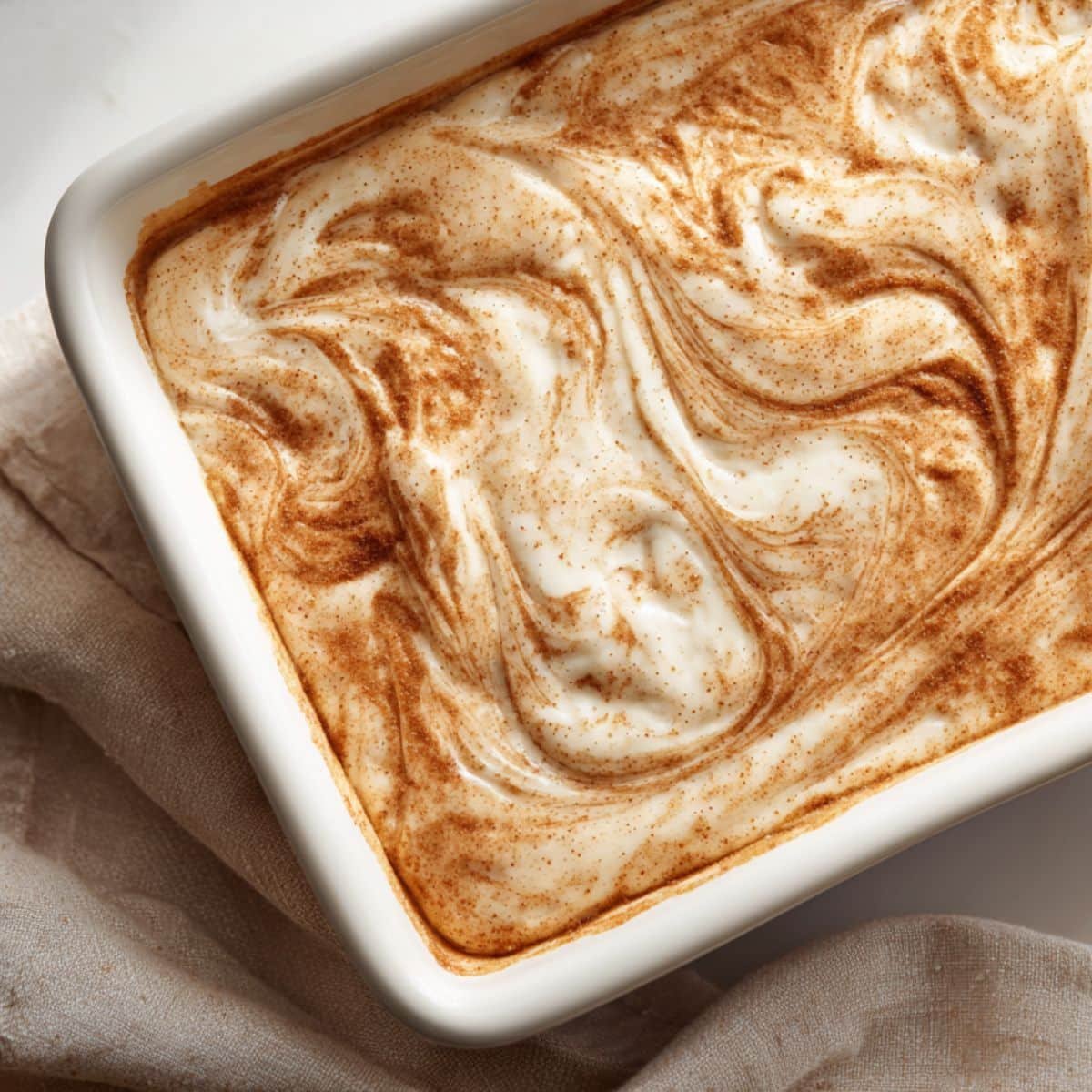 Swirling cinnamon sugar into cake batter in white pan	