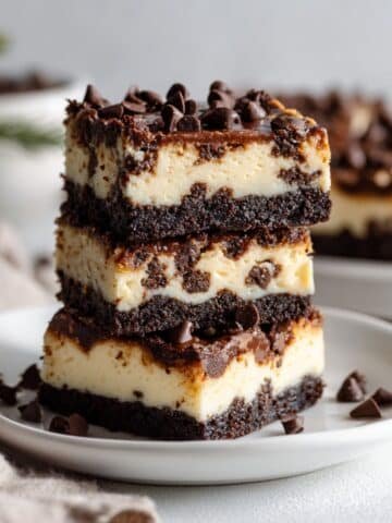 Stack of homemade chocolate chip cheesecake bars with cookie crust and mini chocolate chips on top, placed on a white plate.
