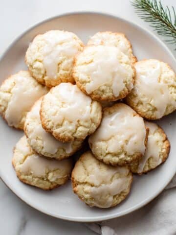 Freshly baked glazed Italian anise cookies on a white plate, photographed top-down in a bright white kitchen.