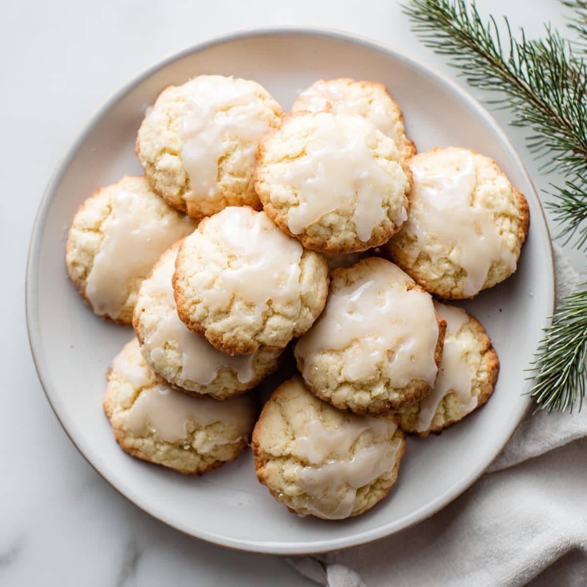 Freshly baked glazed Italian anise cookies on a white plate, photographed top-down in a bright white kitchen.
