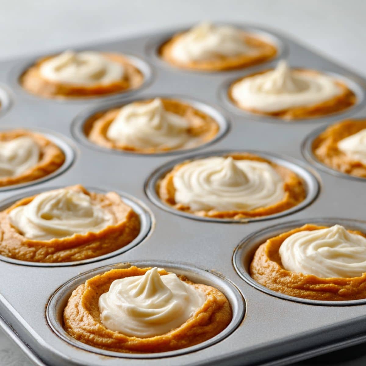 Muffin tin filled with batter and cream cheese swirl before baking