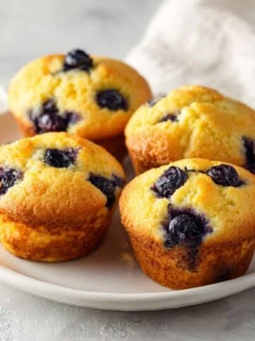 Freshly baked blueberry cornbread muffins on a white kitchen counter, golden tops with blueberries, homemade cozy look