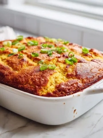 Homemade chili and cornbread casserole baked golden brown with green onion garnish in a white kitchen