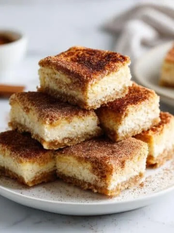 Stack of homemade churro cheesecake bars on white plate