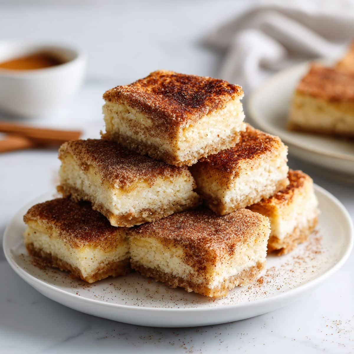Stack of homemade churro cheesecake bars on white plate