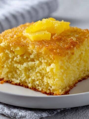 Moist crushed pineapple cake slice with cream cheese frosting on white plate in bright kitchen