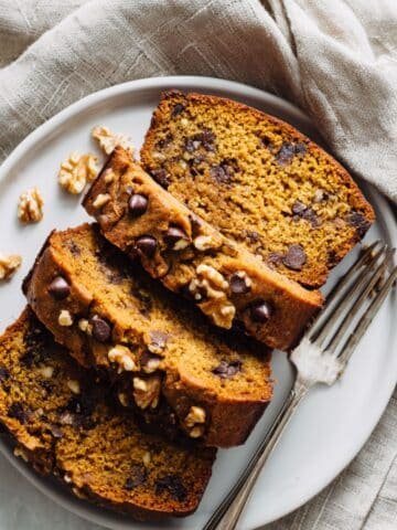 Homemade pumpkin banana bread loaf sliced with chocolate chips and walnuts on a white counter
