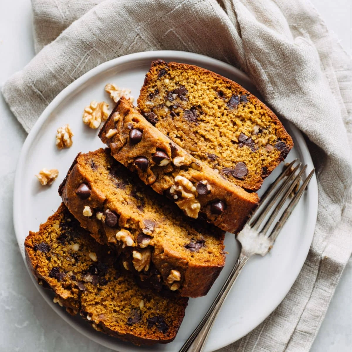 Homemade pumpkin banana bread loaf sliced with chocolate chips and walnuts on a white counter