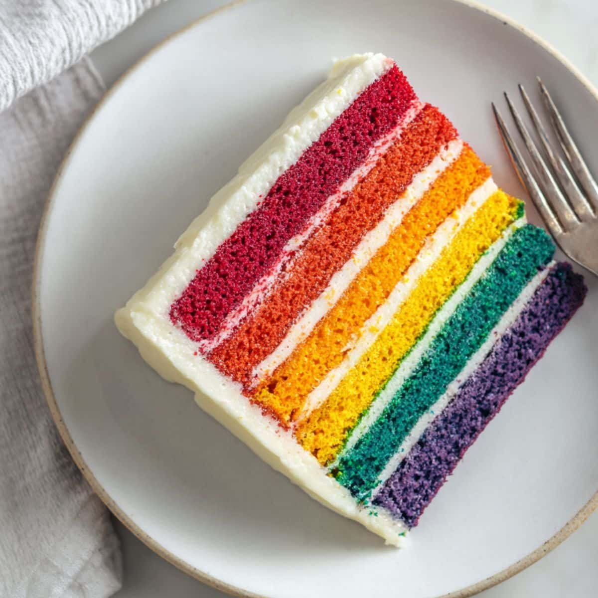 Homemade rainbow cake slice on a plate with colorful layers
