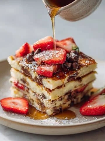 Stack of sheet pan pancakes with strawberries and syrup on a white plate