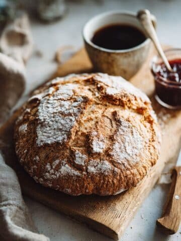 Rustic homemade gluten-free peasant bread loaf sliced on a wooden board with jam and coffee
