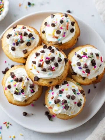 Top-down photo of homemade frosted mini cakes with sprinkles and chocolate chips on a white kitchen counter