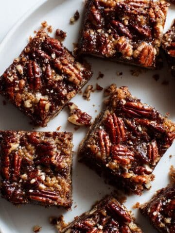 Top-down photo of gooey pecan pie brownies with caramelized pecan topping on a white kitchen table.